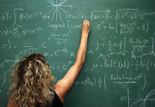 A shot of the back of a female teacher writing equations on a blackboard