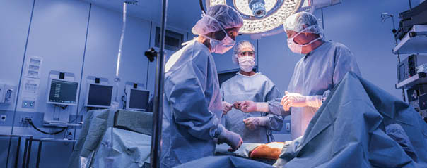 Doctors wearing surgical masks and gowns performing an operation on a patient in a hospital operating theater.