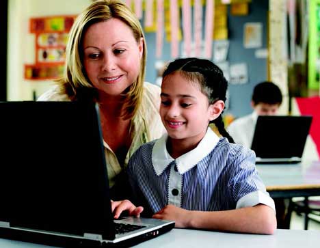 Teacher and schoolgirl using a laptop in a classroom